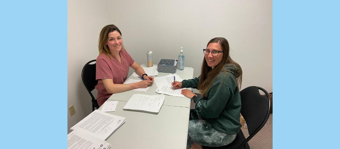 Une professionnelle de la santé (Anne-Élisabeth Roy-Pothier) et une participantes, sont souriantes assises à une table et semblent remplir un formulaire